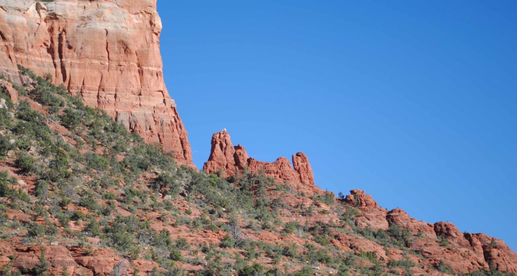 Red rock cliffs and buttes in Sedona, Arizona, rising above sparse desert vegetation under a clear blue sky.