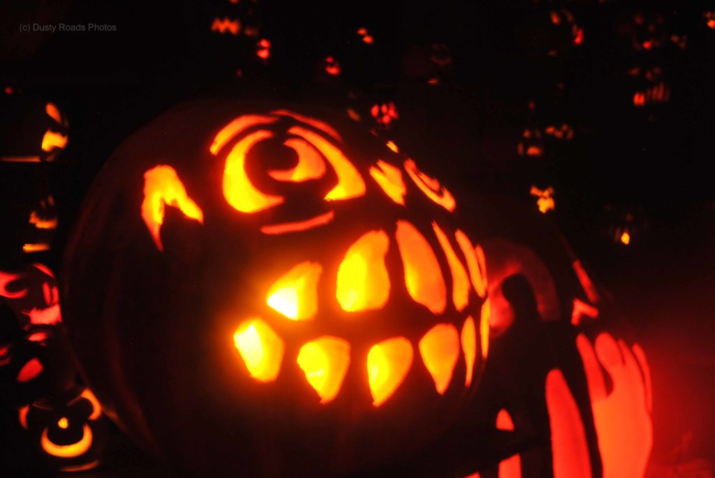 A glowing carved pumpkin with large eyes and a wide toothy grin, surrounded by other illuminated jack‑o’‑lanterns creating a warm, festive Halloween display.