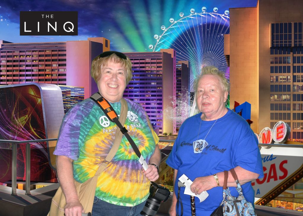 Two visitors posing in front of a colorful LINQ backdrop featuring the illuminated High Roller Ferris wheel and Las Vegas hotel lights.
