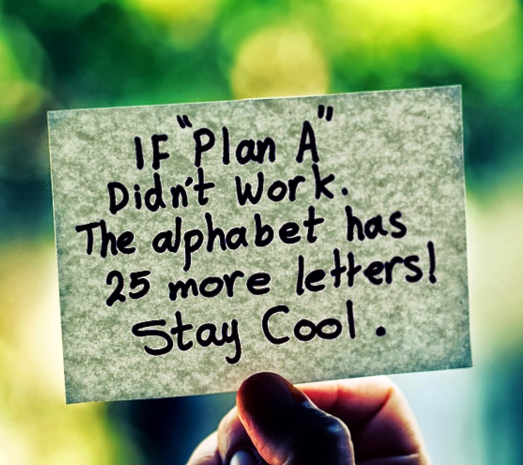 A hand holds a small paper note with a motivational message about Plan A and the alphabet, against a softly blurred green‑blue background.