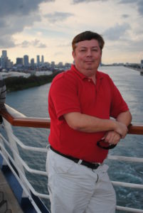 Man in red shirt leans on railing by the ocean