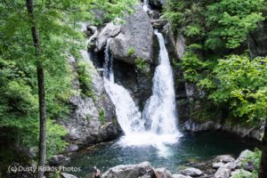 Waterfall cascading over large rocks into a clear pool, surrounded by lush green forest at Bash Bish Falls.”