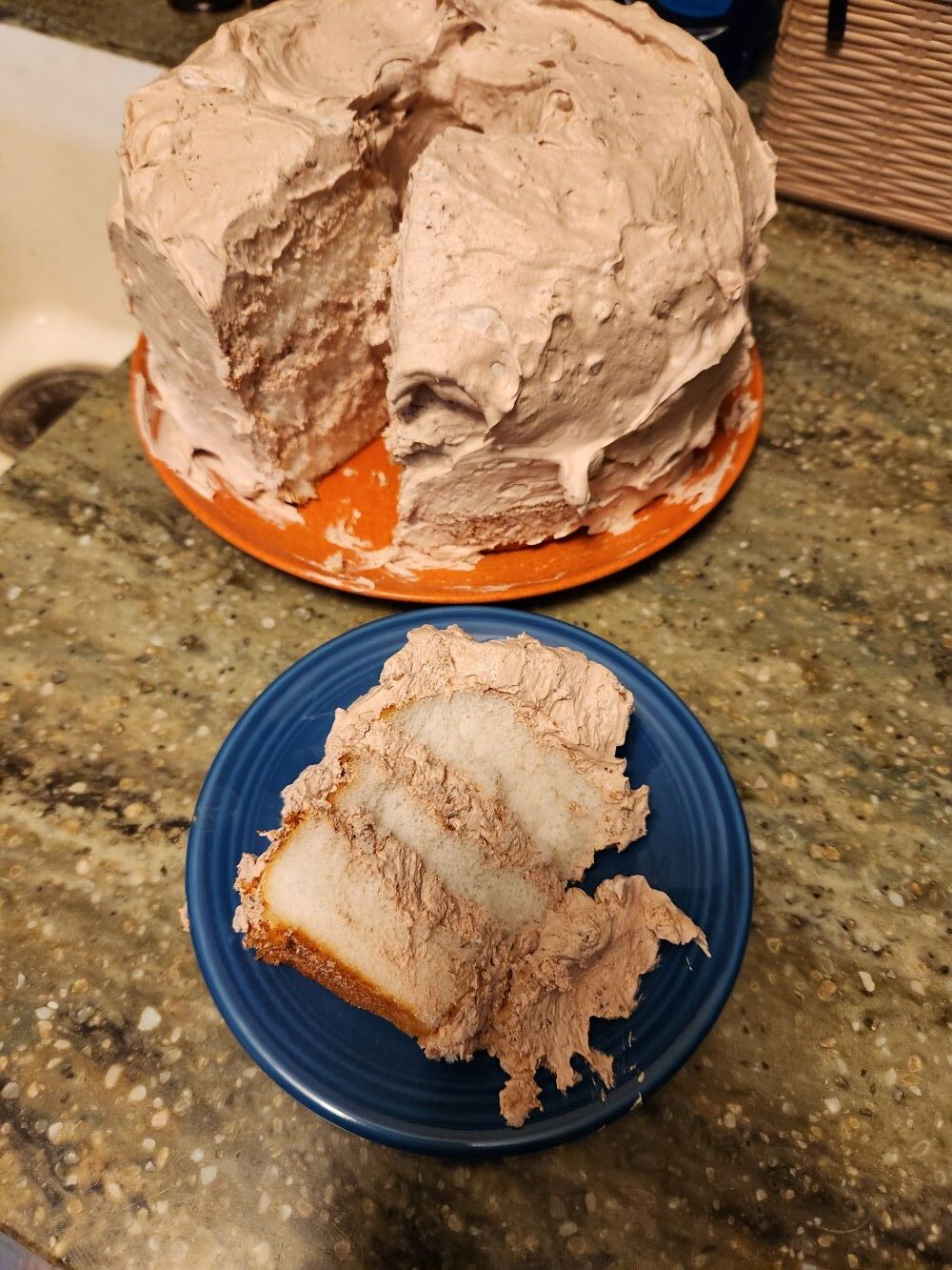 Partially sliced angel food cake covered in light toffee‑flavored whipped topping, with a single slice served on a blue plate.