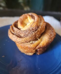 Freshly baked cruffin with crisp, swirled layers and cinnamon sugar on a blue plate.