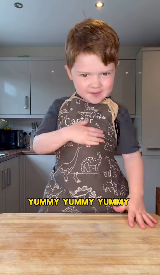 Kid chef Carter in a dinosaur apron at the kitchen counter, happily declaring ‘Yummy, yummy, yummy’ during one of his cooking videos.