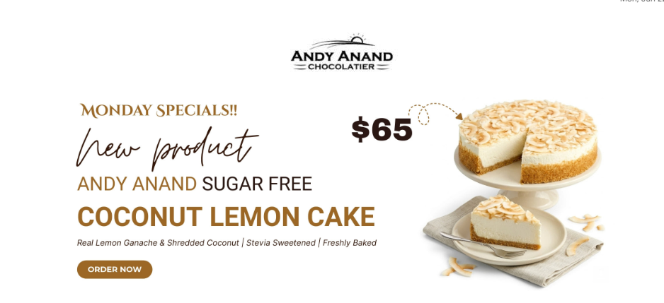 A sugar‑free coconut lemon cake on a white cake stand with a slice cut out, showing the moist lemon ganache and shredded coconut topping. A plated slice sits beside it with a fork and napkin, part of an Andy Anand Chocolatier Monday Special advertisement.