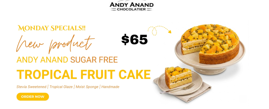 Sugar‑free tropical fruit cake from Andy Anand Chocolatier, shown whole with a slice on a plate, topped with bright tropical fruit and glaze, promoted as a Monday Special.