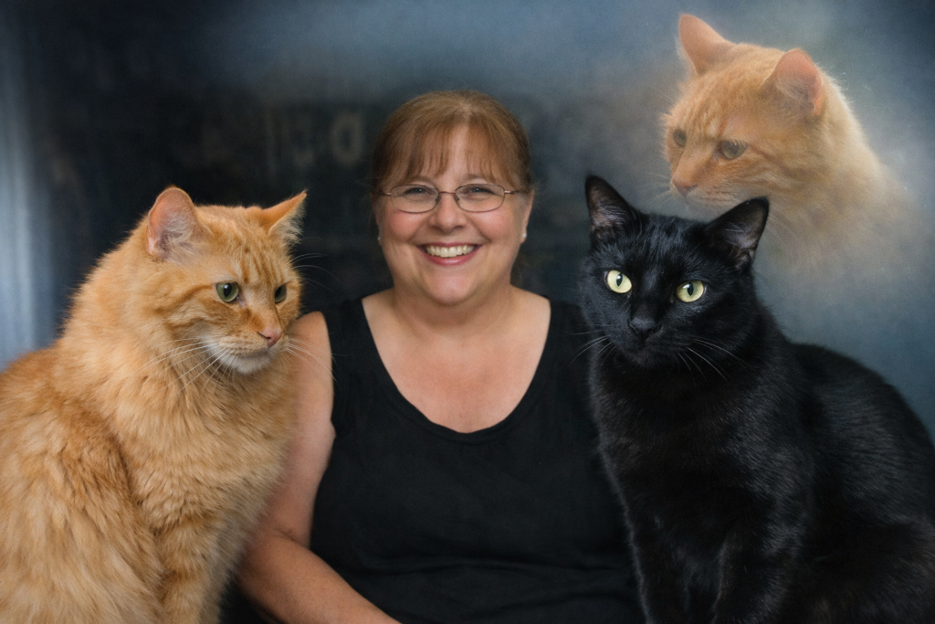“Deborah sits between her two cats, Banner (orange tabby) and Balboa (black cat), with a softly glowing, ethereal image of her retired editor‑in‑chief cat Rocky in the upper right corner.”