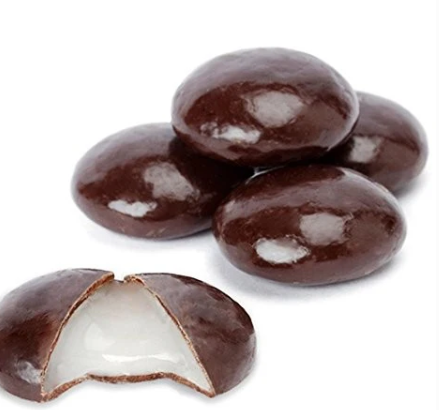 Five glossy chocolate Junior Mints candies arranged on a white surface, with one cut open to reveal the smooth white mint filling.