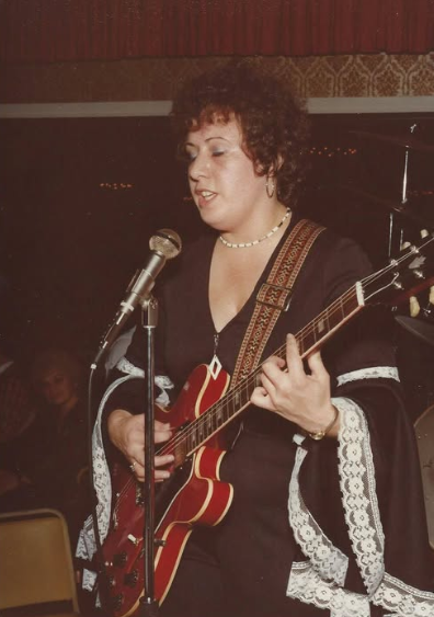 “Me performing onstage with my red electric guitar, singing into the microphone. I’m wearing a black outfit with white lace sleeves and a pearl necklace, completely lost in the music. I loved that guitar — still can’t believe I ever let it go.”