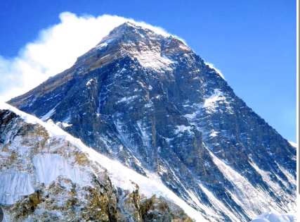 Snow‑covered summit of Mount Everest under a clear blue sky, with wind blowing a small plume of snow from the peak.