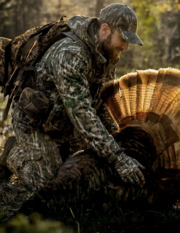 Hunter wearing full camo clothing and holding a turkey,
