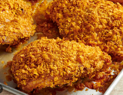 Crispy baked chicken pieces coated in a golden cornflake crust, arranged on a metal baking sheet with an evenly browned, crunchy texture.