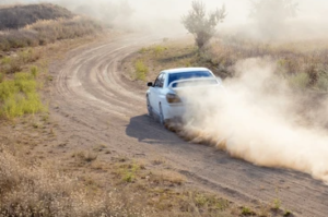 Car traveling on a dirt road with dust billowing out behind it