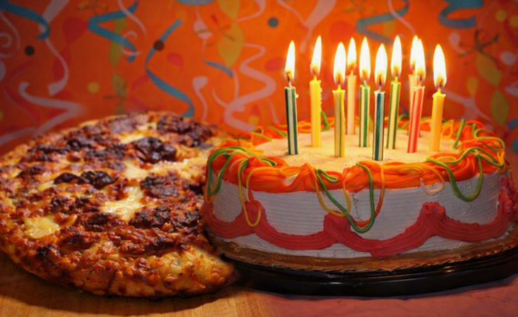 “Festive birthday scene featuring a round cake with orange, red, and green frosting swirls and lit multicolored candles beside a thick‑crust pepperoni pizza with melted cheese and browned toppings, set against a bright orange background with colorful streamers and confetti.”
