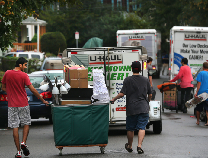 Students and families unloading belongings from multiple U‑Haul trucks on a Boston residential street during fall move‑in day.