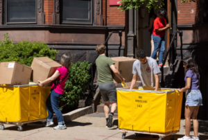 Students pushing large BU Housing carts and carrying boxes outside a campus residence hall during Boston move‑in day.