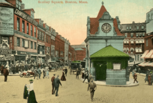 A historic street scene of Scollay Square shows people walking along cobblestone roads with horse‑drawn carriages and early automobiles. A small building with a clock tower and a red‑tiled roof stands at the center, surrounded by brick storefronts and vintage signs, capturing the lively atmosphere of early 20th‑century Boston.