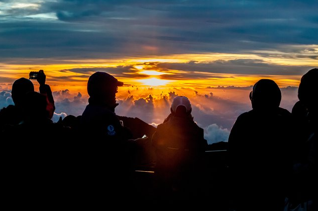   
“Silhouetted group of people watching a dramatic sunrise above a glowing cloud layer, with golden and orange light illuminating the sky.”