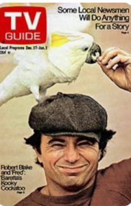 A man wearing a brown cap and jacket holds a white cockatoo perched on his head as the bird pecks at his finger on the cover of a TV Guide magazine featuring Robert Blake and his cockatoo from the show “Baretta.”