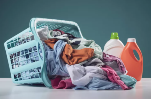 Tipped-over laundry basket with colorful clothes spilling out beside two detergent bottles on a white surface.