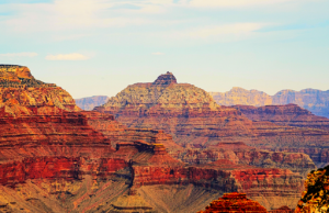  Red sandstone cliffs and buttes rise above the town of Sedona, Arizona, with green trees and scattered houses in the foreground under a partly cloudy sky.