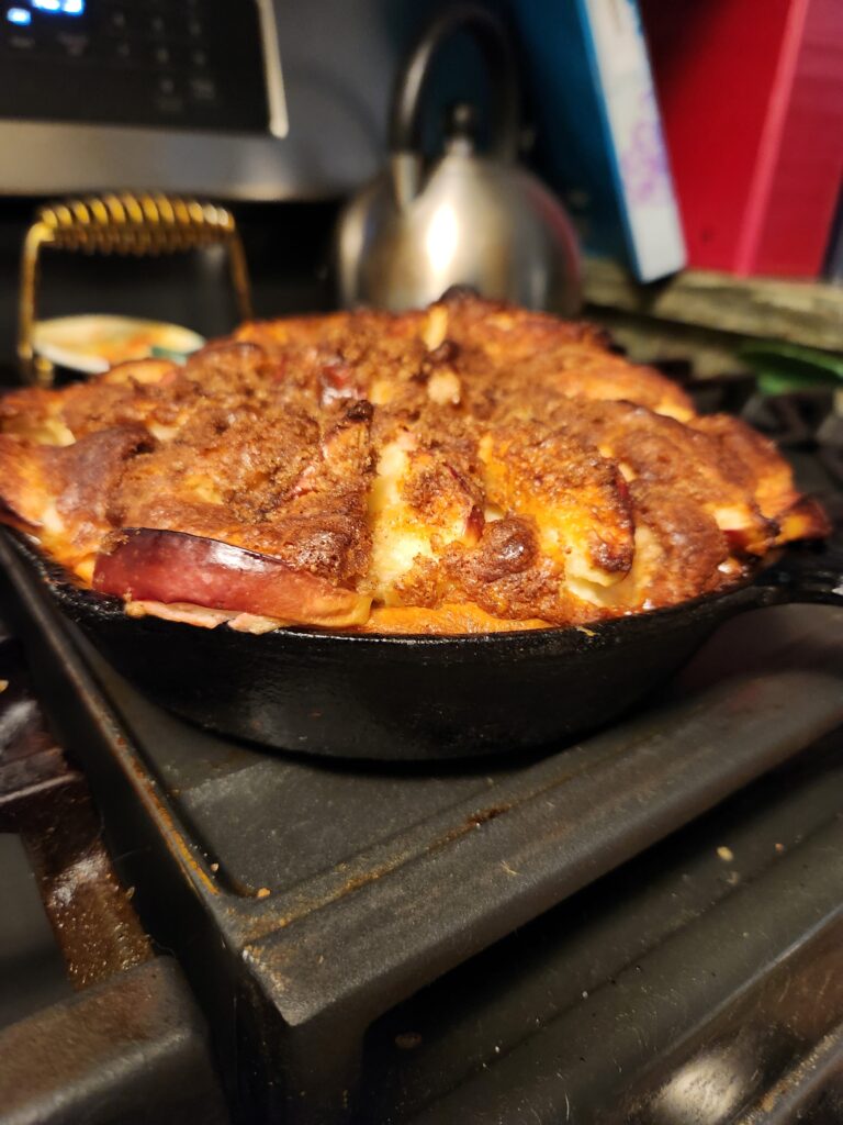 Golden, deep‑dish apple pancake baked in a black cast‑iron skillet, with a caramelized top and crisp browned edges.