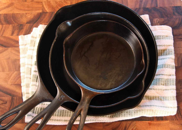 Three cast iron skillets of different sizes stacked inside one another on a striped kitchen towel resting on a wooden countertop.