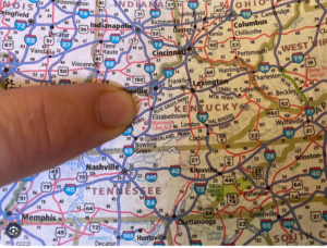 “Close-up of a printed road map showing parts of Kentucky, Tennessee, Indiana, and Ohio, with a finger pointing near Louisville.”