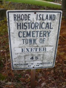 Weathered metal cemetery marker lying among fallen leaves and grass, identifying a historical burial site in Exeter, Rhode Island.