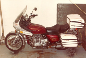   
A vintage maroon-and-white Honda Gold Wing motorcycle with a large Windjammer III fairing and hard saddlebags sits parked indoors on a concrete floor, showing detailed pinstriping and chrome engine components.