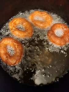 Four golden‑brown donuts float in bubbling hot oil as they finish frying in a deep pan.