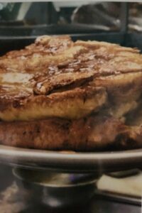 Close‑up of a thick, golden‑brown apple pancake stacked on a plate, with a glossy surface from syrup or melted butter, photographed in a warm kitchen setting.
