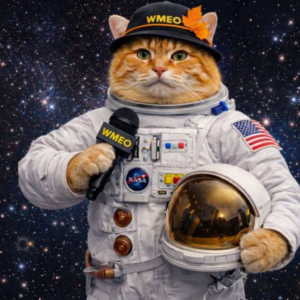 Pumpkin Spice, an orange cat dressed in a white astronaut suit, holds a gold‑visored helmet under one arm and a WMEO microphone in the other. He wears a black WMEO press hat with an orange leaf, standing against a starry outer‑space background.