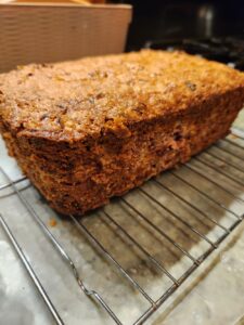 “Freshly baked fruit loaf with a golden, textured crust cooling on a metal rack over parchment paper.”