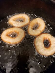 Four ring‑shaped donuts fry in bubbling hot oil, their edges turning golden brown as they cook.
